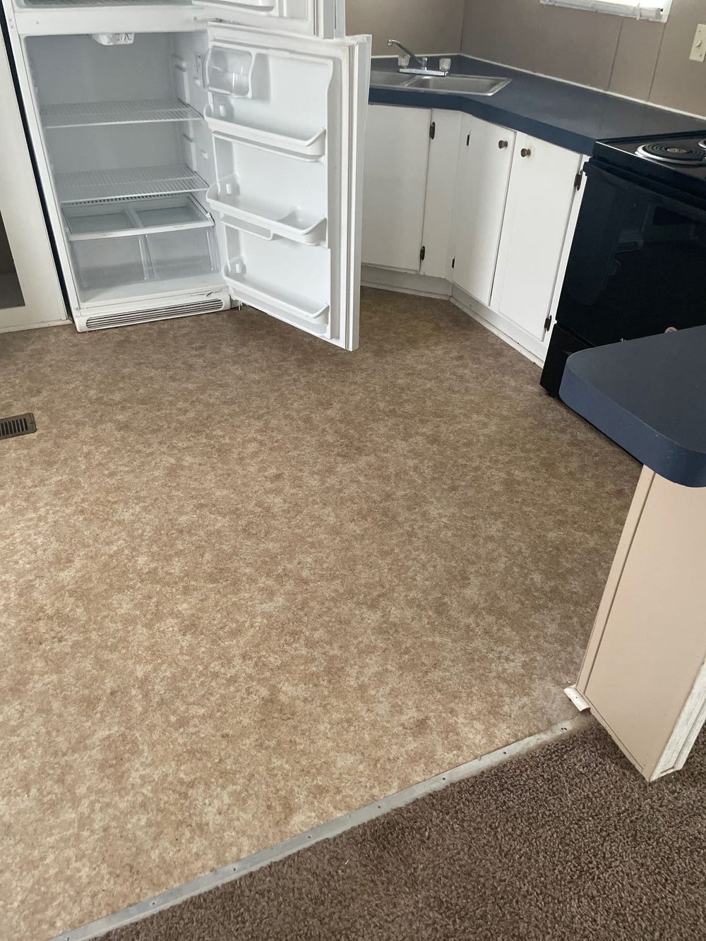 Kitchen before renovation, worn carpet and dated cabinets