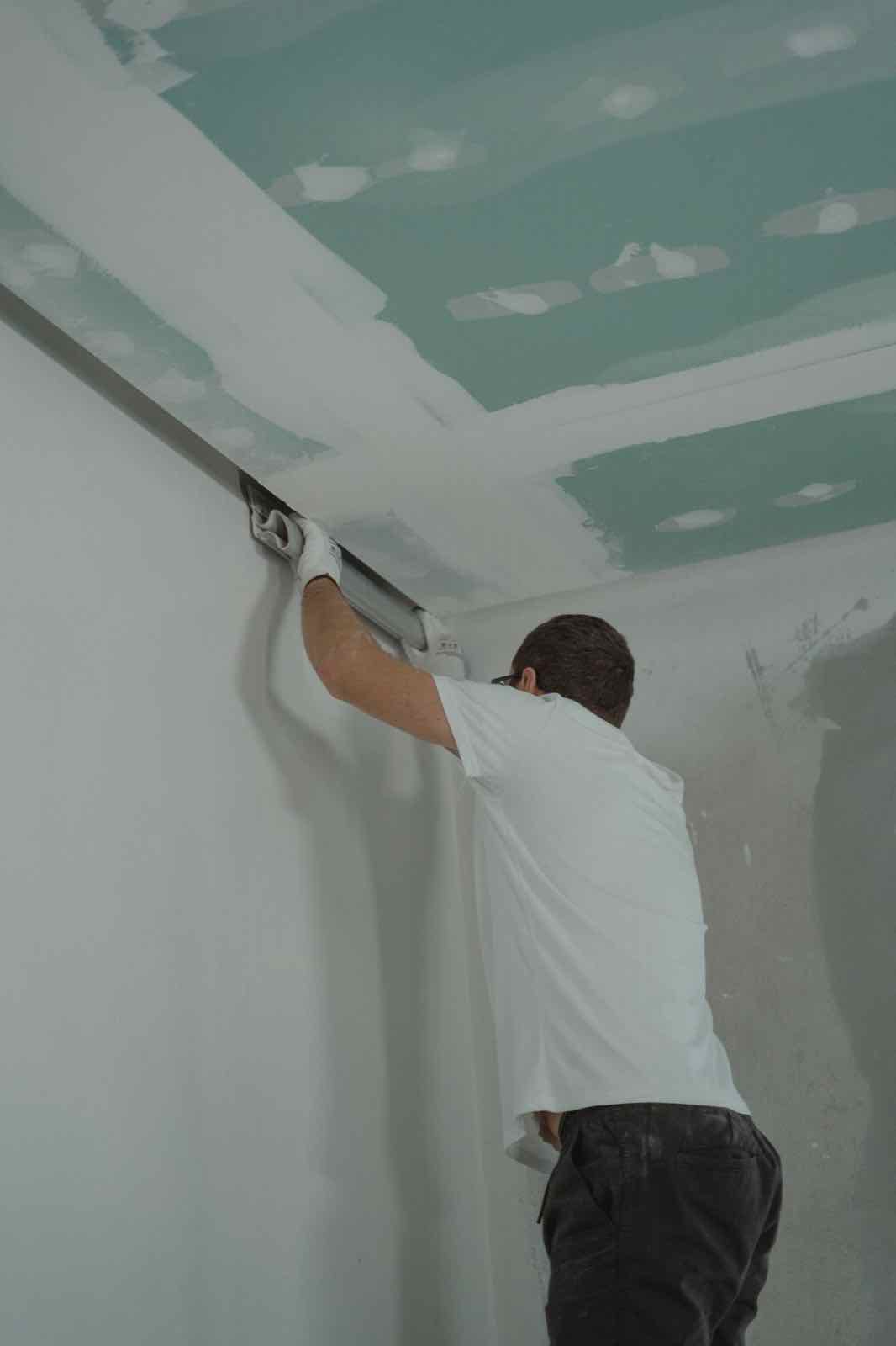 Worker finishing a drywall ceiling seam during a renovation