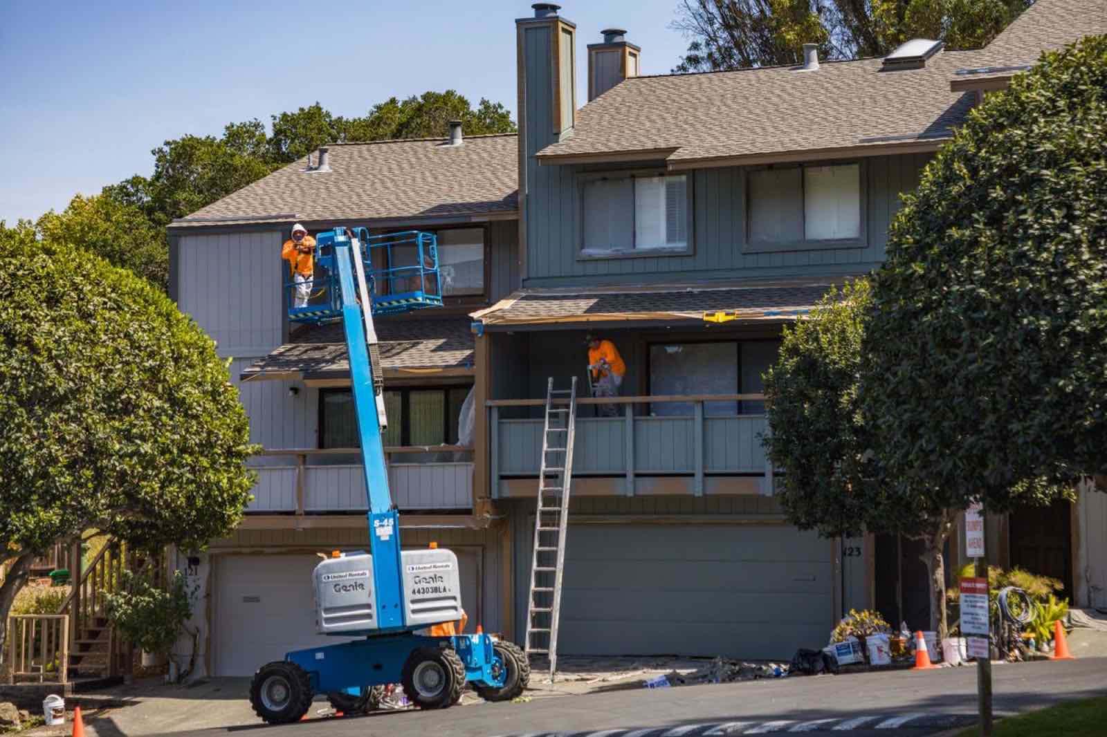 Painters on a lift repainting the exterior siding of a house